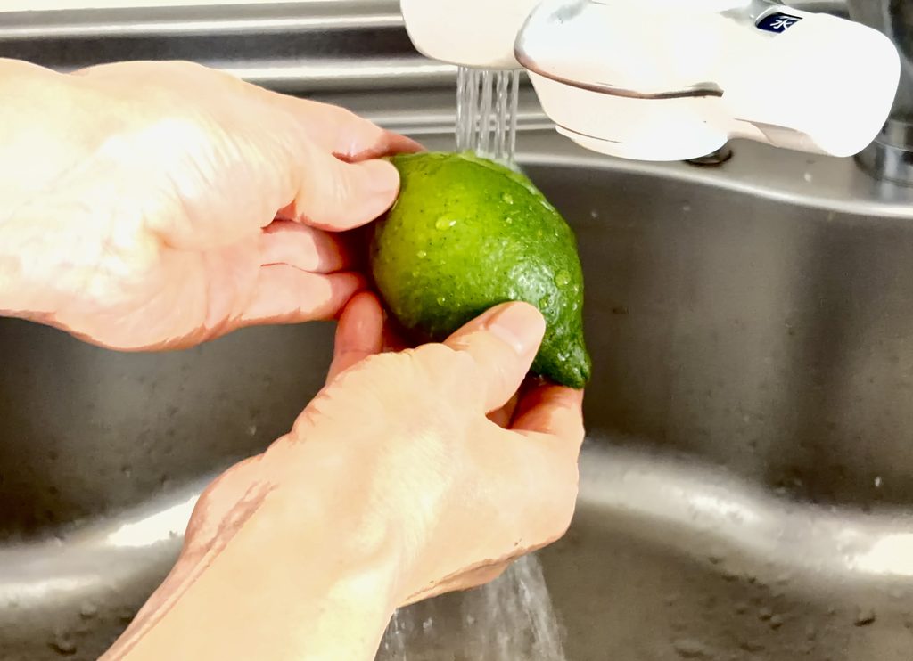 流水で緑色のレモンを洗っている手元